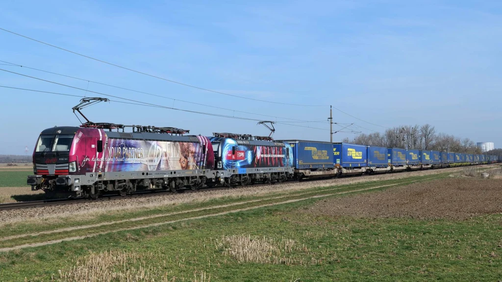 Adesso Rail Güterzug mit buntem Branding-Wrap fährt durch eine ländliche Landschaft