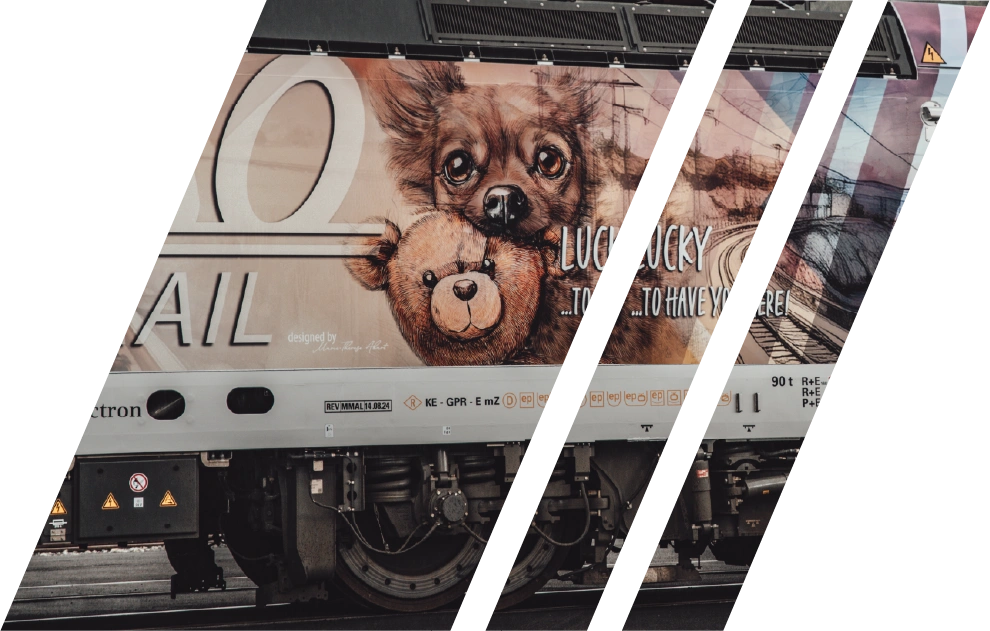 Lokomotive mit künstlerischem Ganzkörper-Wrapping: Das Motiv zeigt einen braunen Hund mit einem Teddybär sowie den Schriftzug „Lucky to have you here!" Die Aufnahme ist diagonal durch weiße Schrägstriche unterteilt, der Hintergrund ist transparent.